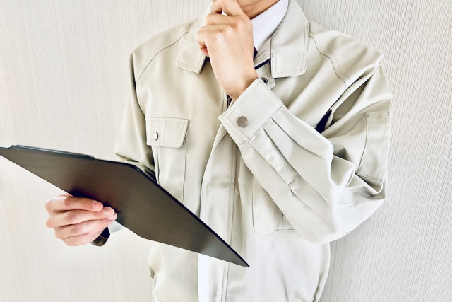 作業服を着た人物が考えながらクリップボードを持つ図